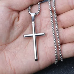 Detailed view of a small polished silver cross pendant on a box chain held in hand
