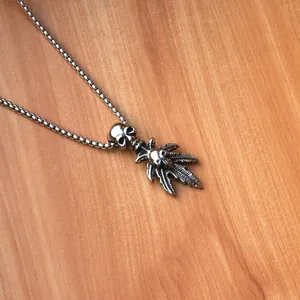 Detail of vintage silver skull and maple leaf pendant on a stainless steel box chain