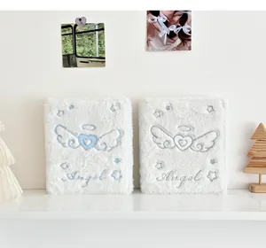 Detalle de álbum de fotos A6 de peluche con bordado de alas de ángel y textura de piel blanca