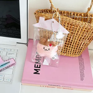 Llavero de gato de peluche rosa con cereza en una funda transparente con forma de casa