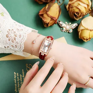 Women's rose gold rectangular watch with diamond bezel and red leather strap on green background