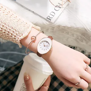 Detail shot of women's oval white dial watch with brown leather strap and rose gold jewelry