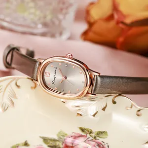 Detailansicht der ovalen Roségold-Quarzuhr mit schmalem Lederarmband auf floralem Teller