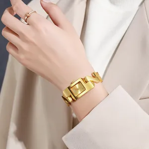 Detail van goudkleurig horloge en emaille ring gedragen bij een beige kostuum