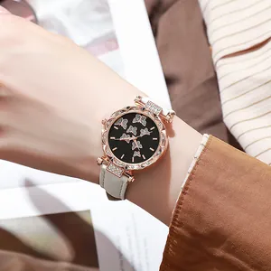 Detail of elegant rose gold watch with rhinestone butterflies on black dial and cream strap