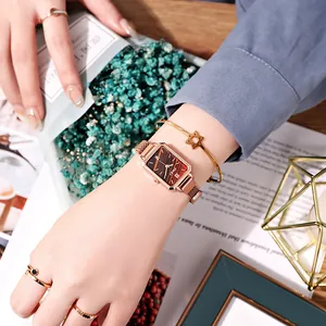 Detail of rose gold rectangular watch with wood texture dial and mesh bracelet on wrist