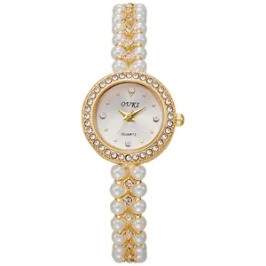 Detailed macro view of an elegant gold quartz watch with pearl bead bracelet and rhinestones