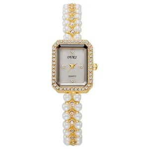 Close-up of rectangular gold watch case with diamond bezel and pearl chain strap