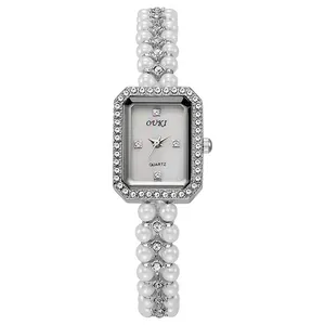 Macro view of rectangular mother-of-pearl watch face with crystal bezel and pearl strap