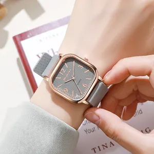 Detail of square rose gold watch with grey silicone strap on wrist over a magazine