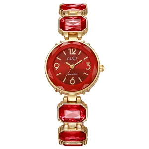 Détail d'une montre dorée avec cadran rouge et pierres précieuses sur le bracelet