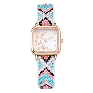 Détail montre carrée or rose avec cadran papillon et bracelet tissé coloré