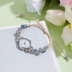 Dettaglio dell'orologio bracciale intrecciato con perline blu e cassa argento su fiori
