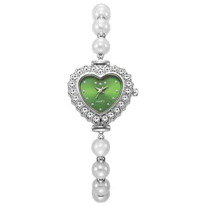 Primer plano de un reloj con esfera verde de corazón con brillantes pedrería y perlas