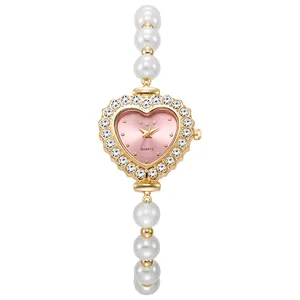 Detalle de reloj dorado con forma de corazón, esfera rosa y pulsera de perlas blancas