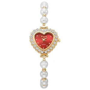 Detalle de reloj dorado en forma de corazón con esfera roja y pulsera de perlas