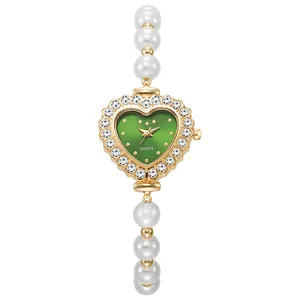 Detalle de reloj dorado de corazón con esfera verde y elegante correa de perlas