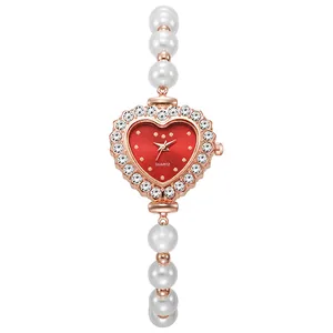 Detalle de reloj corazón oro rosa con esfera roja y correa de perlas blancas