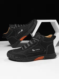 Detail of black leather high-top boots featuring white stitching and orange honeycomb accents