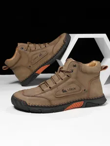 Detail of brown leather boots showing the side logo, stitching, and decorative orange sole insert