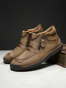 Detail of brown leather men's boot with side zipper, contrast stitching and rubber sole