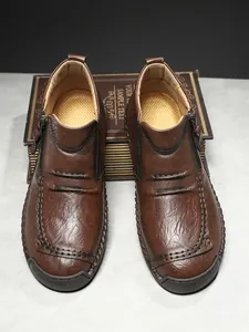 Macro shot of dark brown leather boot with detailed hand stitching and metal zipper side