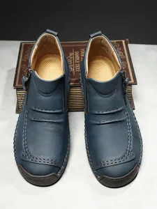 Detail of dark blue leather boots featuring hand-stitched seams and a side zipper