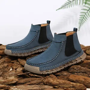 Detail van grijsblauwe suède Chelsea boots met contraststiksel op houten ondergrond