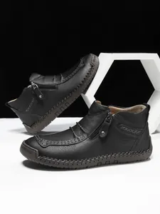 Detail of black leather ankle boot featuring side zipper and decorative hand-stitching