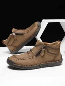 Detail of men's brown suede boots with handmade stitching and side zipper closure