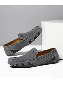 Détail de mocassin en daim gris avec renfort latéral en caoutchouc ondulé et logo élégant