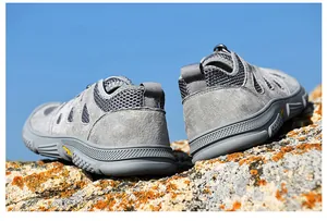 Nahaufnahme grauer Wildleder-Trekkingschuhe mit atmungsaktivem Mesh auf moosigem Fels