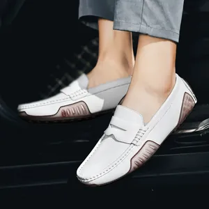 Men's white leather loafers with brown rubber pebble soles in a car interior setting
