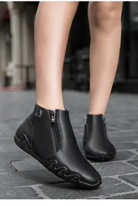 Detail of leather ankle boots featuring a side zipper and decorative metallic deer emblem