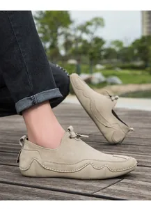 Detalle macro de mocasines de ante caqui con patrones de ondas cosidos a mano sobre madera