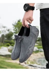 Detalle de mocasín de gamuza gris con cordón decorativo y suela ondulada antideslizante