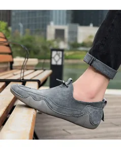 Detalle de mocasines de ante gris con costuras decorativas sobre fondo de madera natural