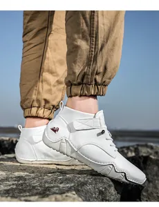 Nahaufnahme weißer High-Top-Freizeitschuh mit Ziegen-Logo und Gummisohle vor Küstenfelsen