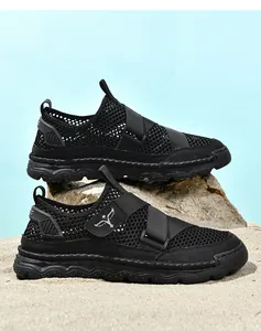 Detail of black mesh sandals on rocks and sand showing breathable texture and non-slip sole