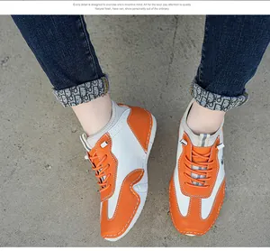 Top view of white and orange lace-up sneakers with perforated leather and stitching
