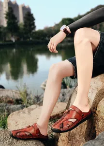 Sandalias de cuero marrón para hombre con costuras a mano y cremallera sobre rocas