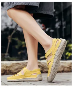 Outdoor side view of yellow hollow-out leather sandals with grey rubber soles and velcro straps