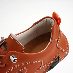 Dettaglio di scarpe in pelle marrone con linguetta arancione e cuciture bianche a contrasto