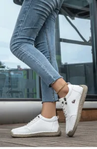 Detail of white handmade stitched flat shoes with side zipper and red ram logo