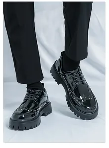 Detailansicht von schwarzen Lackleder-Plateau-Brogues mit Goldnieten und dicken Sohlen