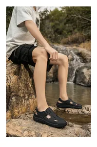 Detail view of men's leather sandals with adjustable strap and stitching on rock