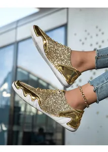 Detailaufnahme goldener Damen-Sneaker mit Pailletten an den Füßen vor moderner Glaswand