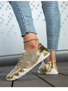 Detail von funkelnden goldenen Pailletten-Sneakern mit Jeans und goldener Fußkette