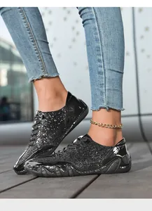 Detail von schwarzen Glitzer-Sneakern mit glänzendem Lackleder an Model in Jeanshose