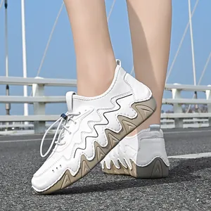 Outdoor perspective view of white leather sneakers with wavy brown sole detail and toggle laces